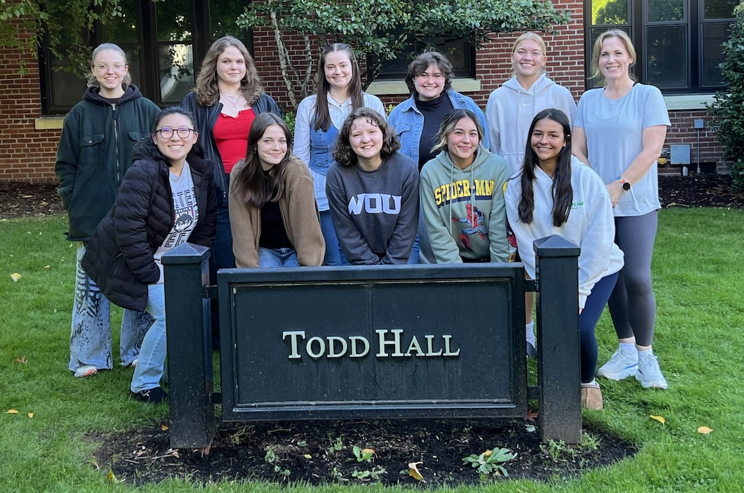 11 Peer Advisors arranged in 2 rows (6 standing in the back and 5 crouching in front) in front of Todd Hall, behind the Todd Hall sign