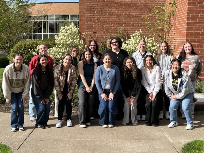Group picture of the Spring Psych PAC Peer Advisors. 15 students (7 standing in the back and 8 slightly squatting in the front) smiling at the camera